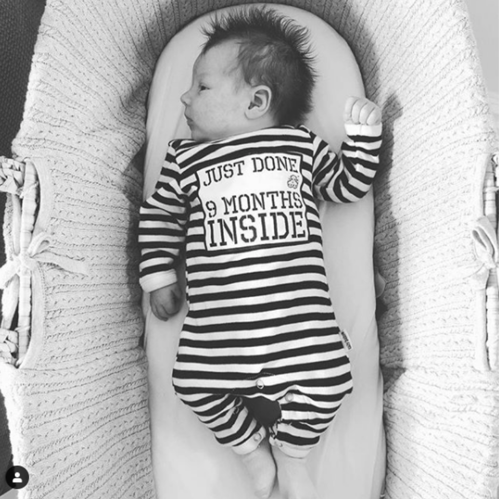 Baby laying in crib wearing Just Done 9 Months Inside baby grow